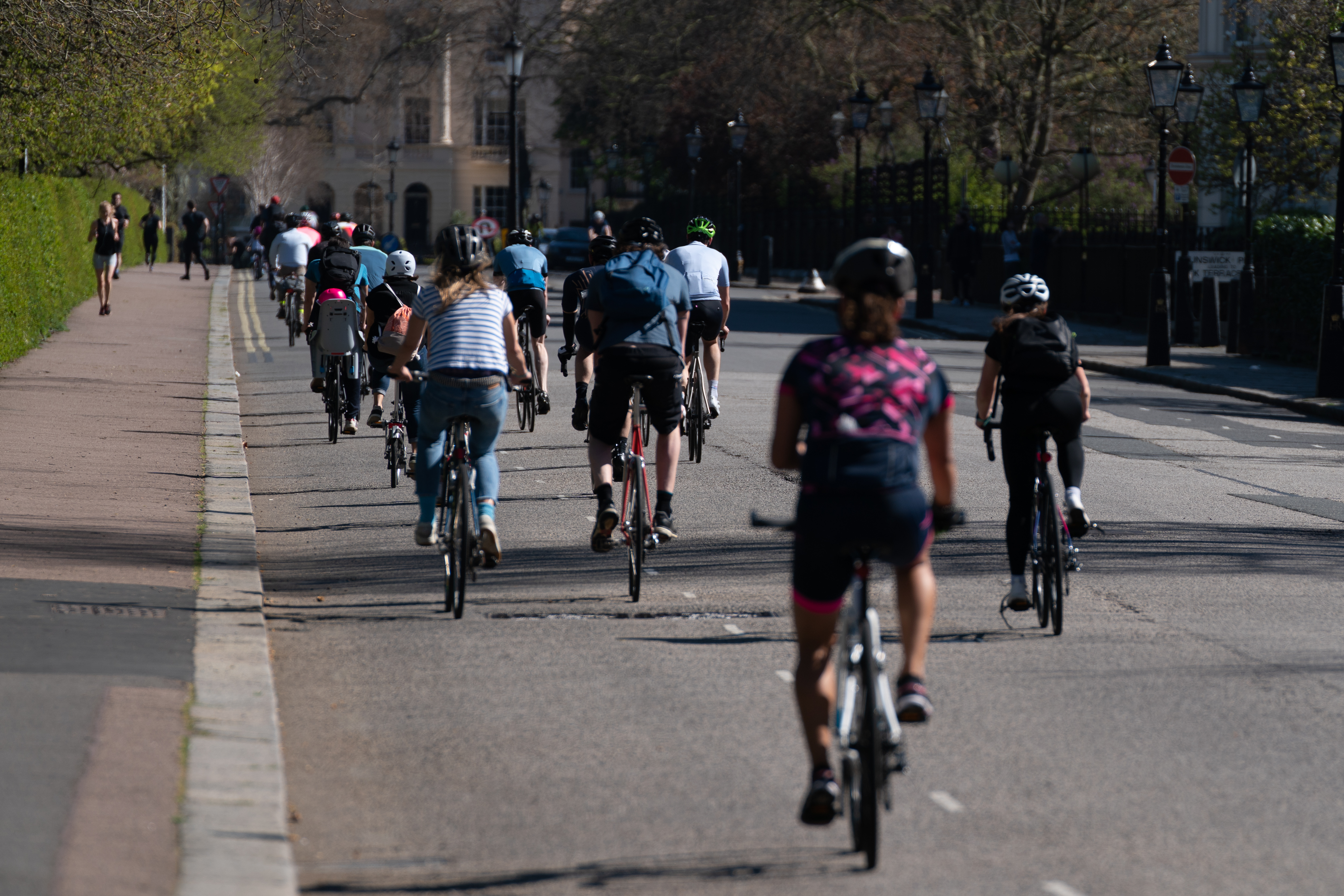 Cyclists riding on a road in Regent's Park, London, with pedestrians on a path to the left.