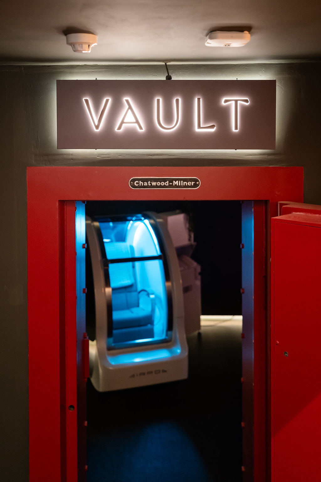 An illuminated "VAULT" sign above a red entrance, revealing a brightly lit, futuristic pod inside.