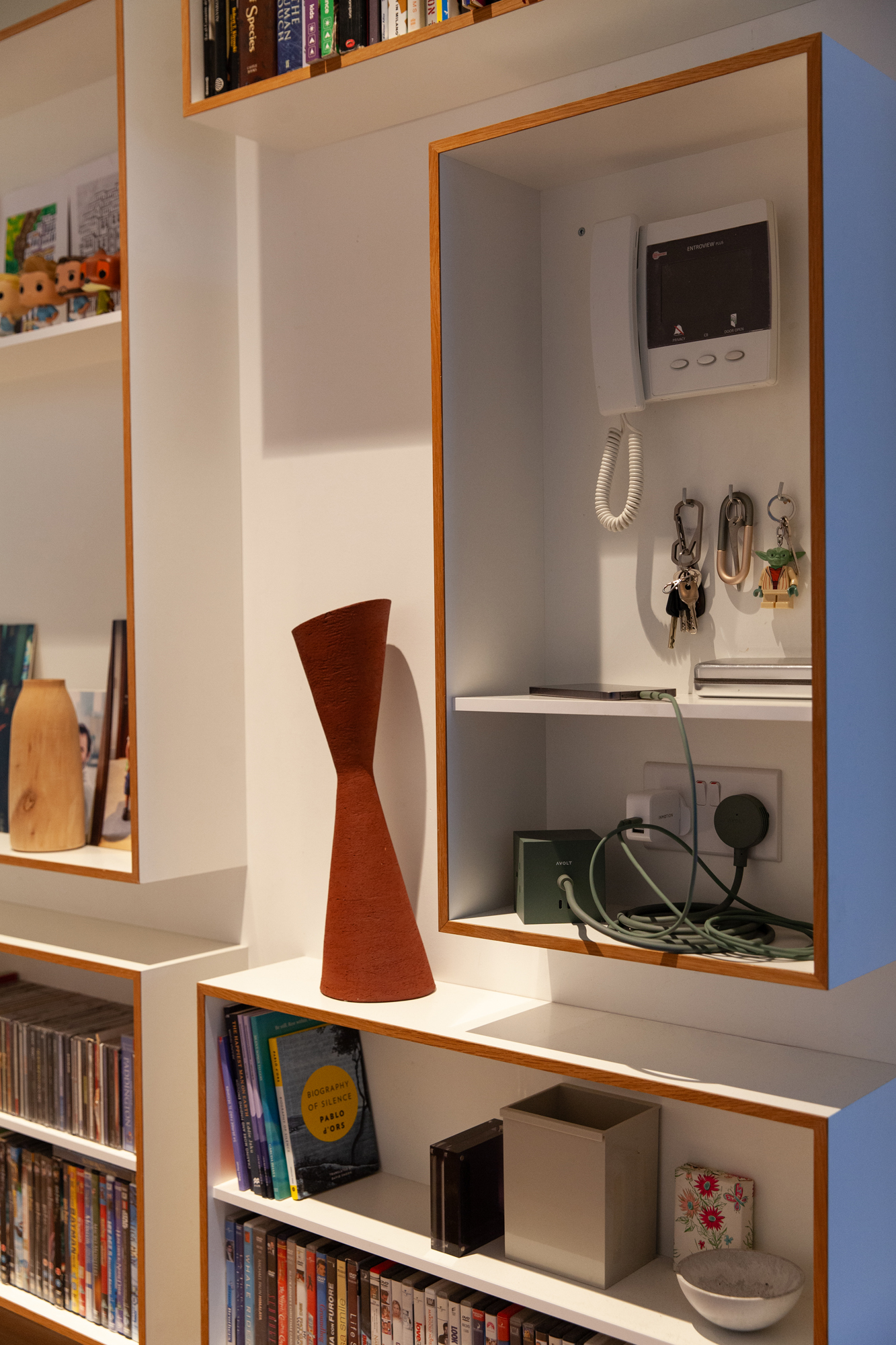 Built-in shelving unit with an intercom, keys, a charging station, books, DVDs, and decor.