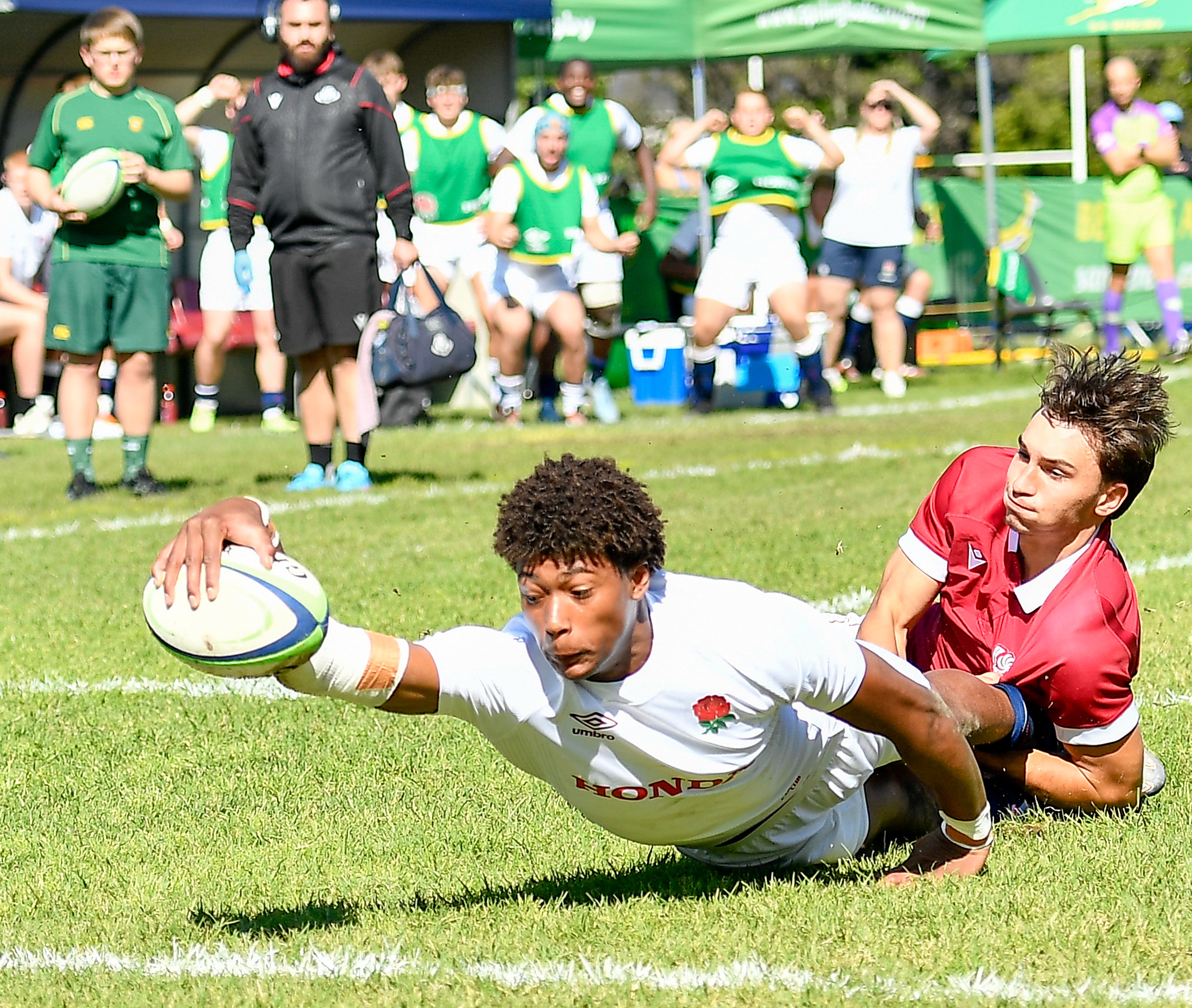 Noah Caluori of England scores a try while being tackled by a Georgian player.