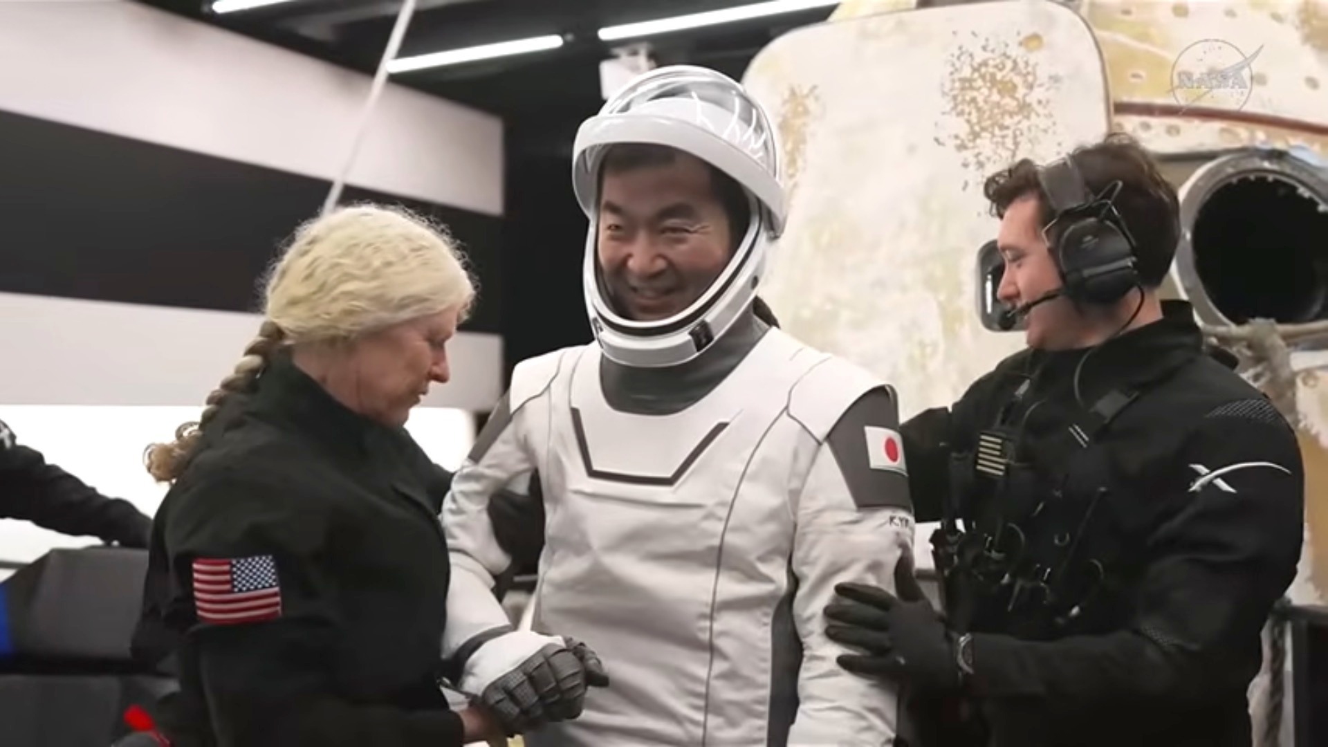 Astronaut Kimiya Yui in a white spacesuit is helped by two crew members after re-entering Earth.