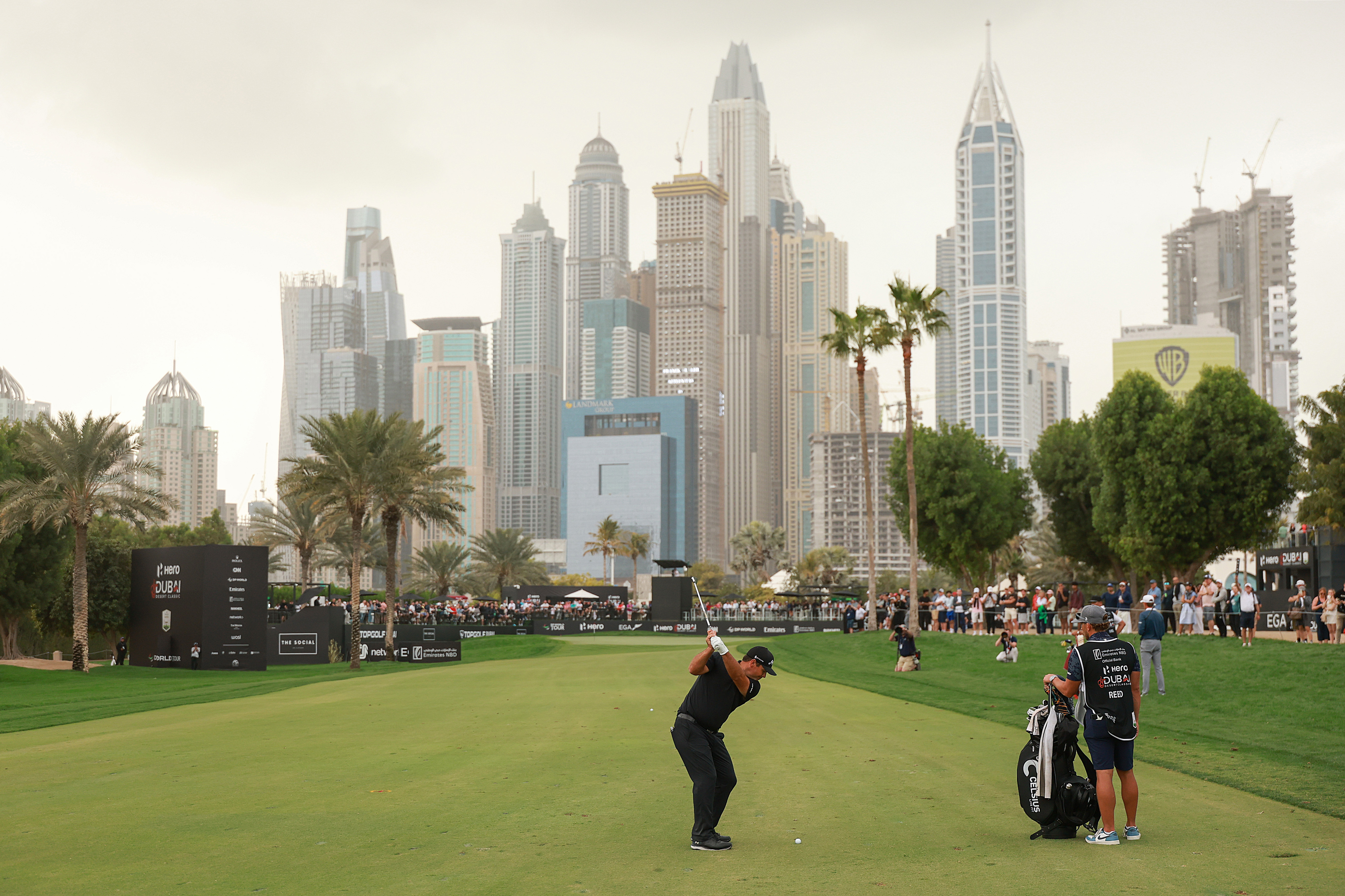 Patrick Reed playing a golf shot with the Dubai skyline in the background.