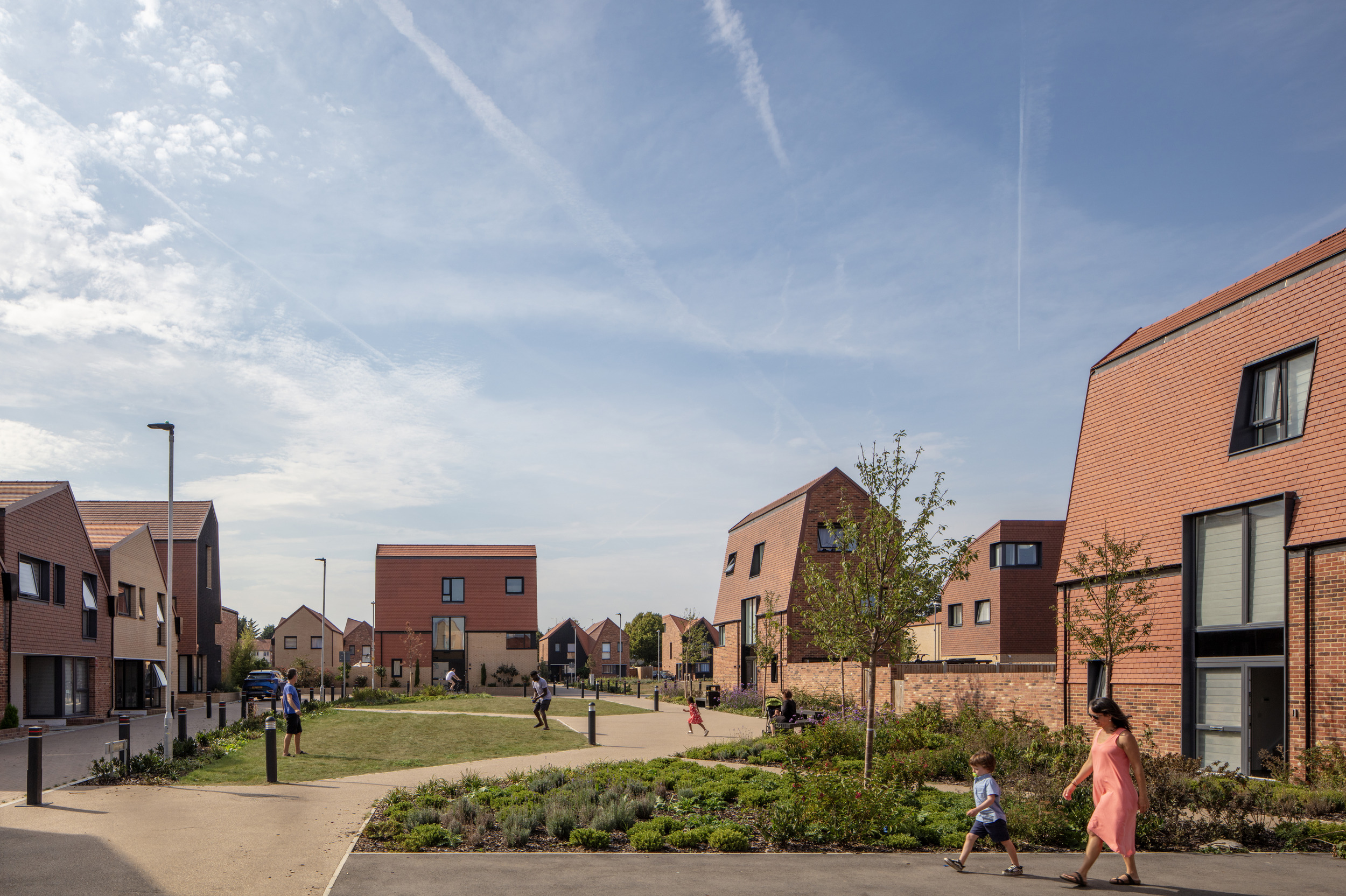 A mixture of contemporary and traditional red-brick homes with families and children walking and playing along accessible pathways and grassy areas.