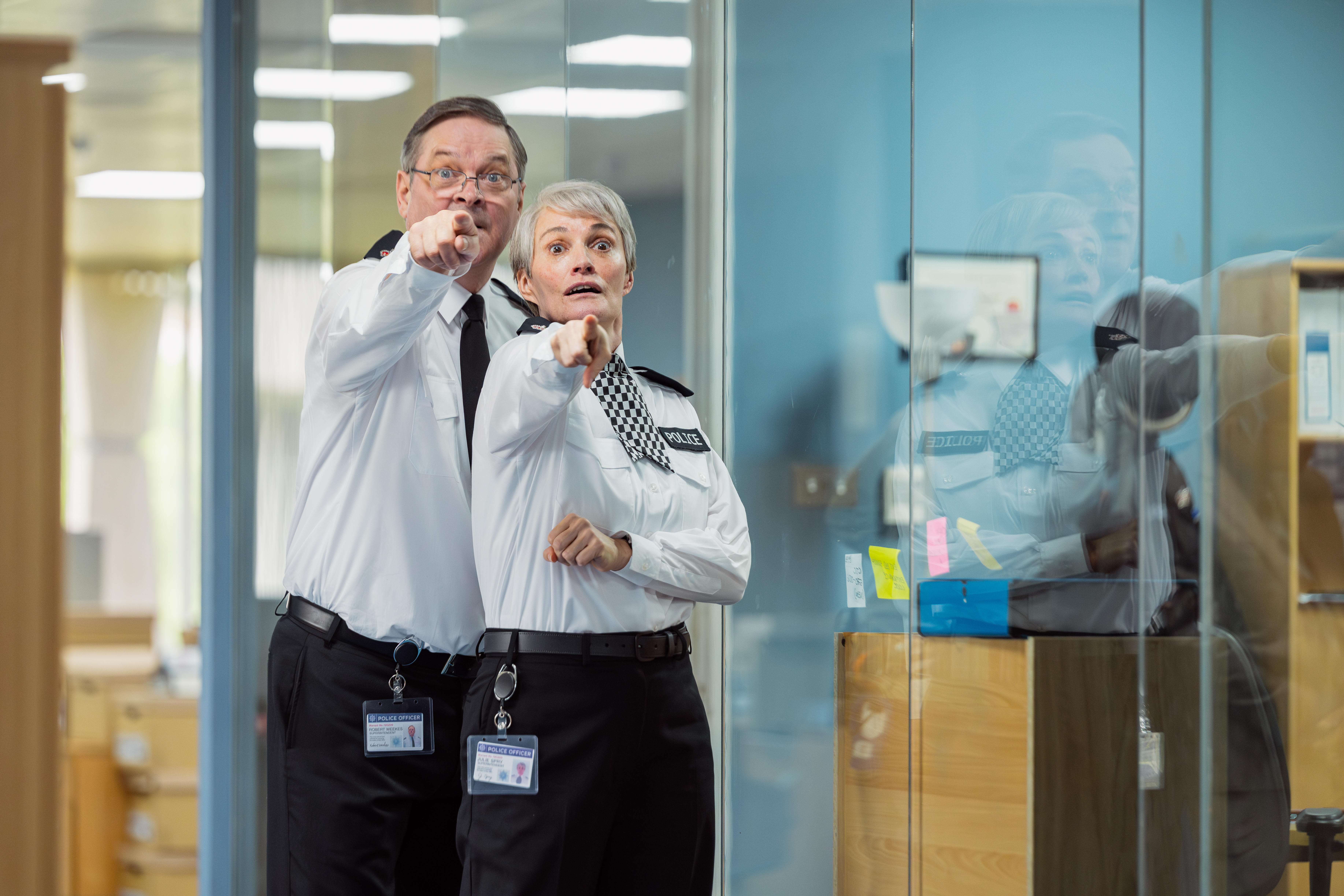 Supt. Bob Weekes (Mark Heap) and Insp. Julie Spry (Sarah Parish) from "Piglets" point directly forward with wide, shocked eyes.