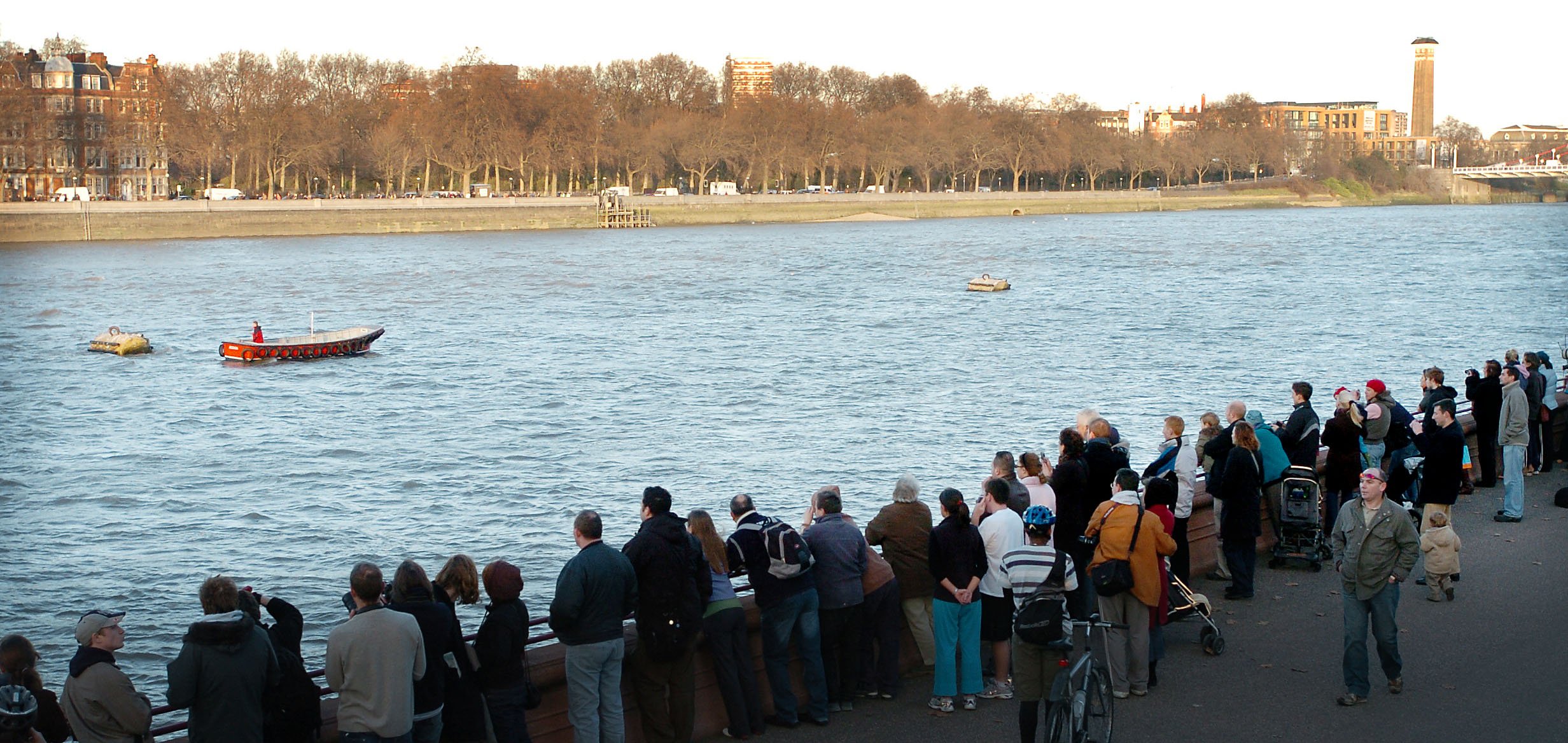 A crowd gathered along the River Thames watching a boat alongside a lost whale.