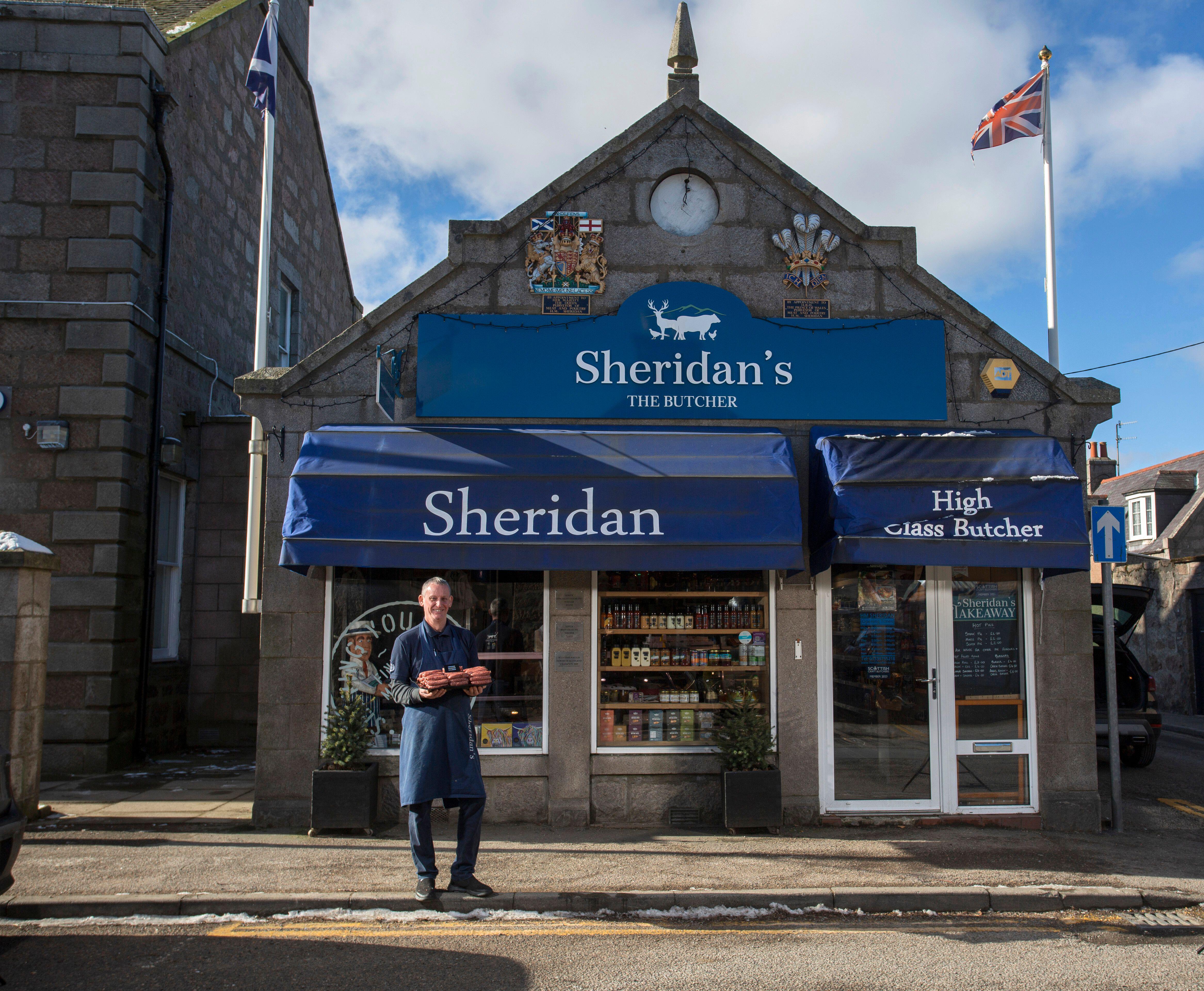 H. M. Sheridan Butchers in Ballater, Aberdeenshire, Scotland, with a man in an apron holding sausages in front of the shop.