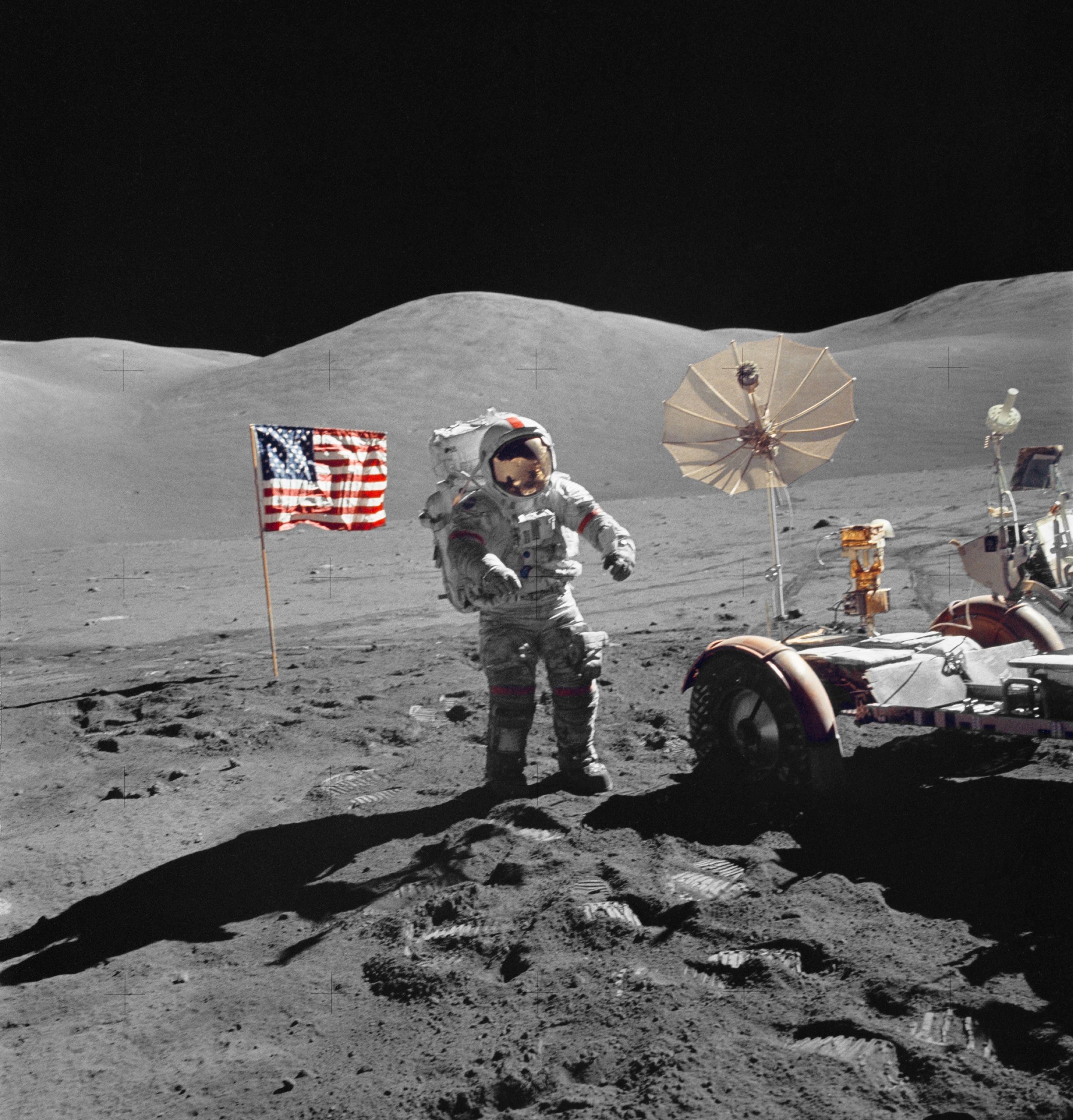 Astronaut Eugene A. Cernan standing next to the Lunar Roving Vehicle with an American flag planted in the background on the Moon.