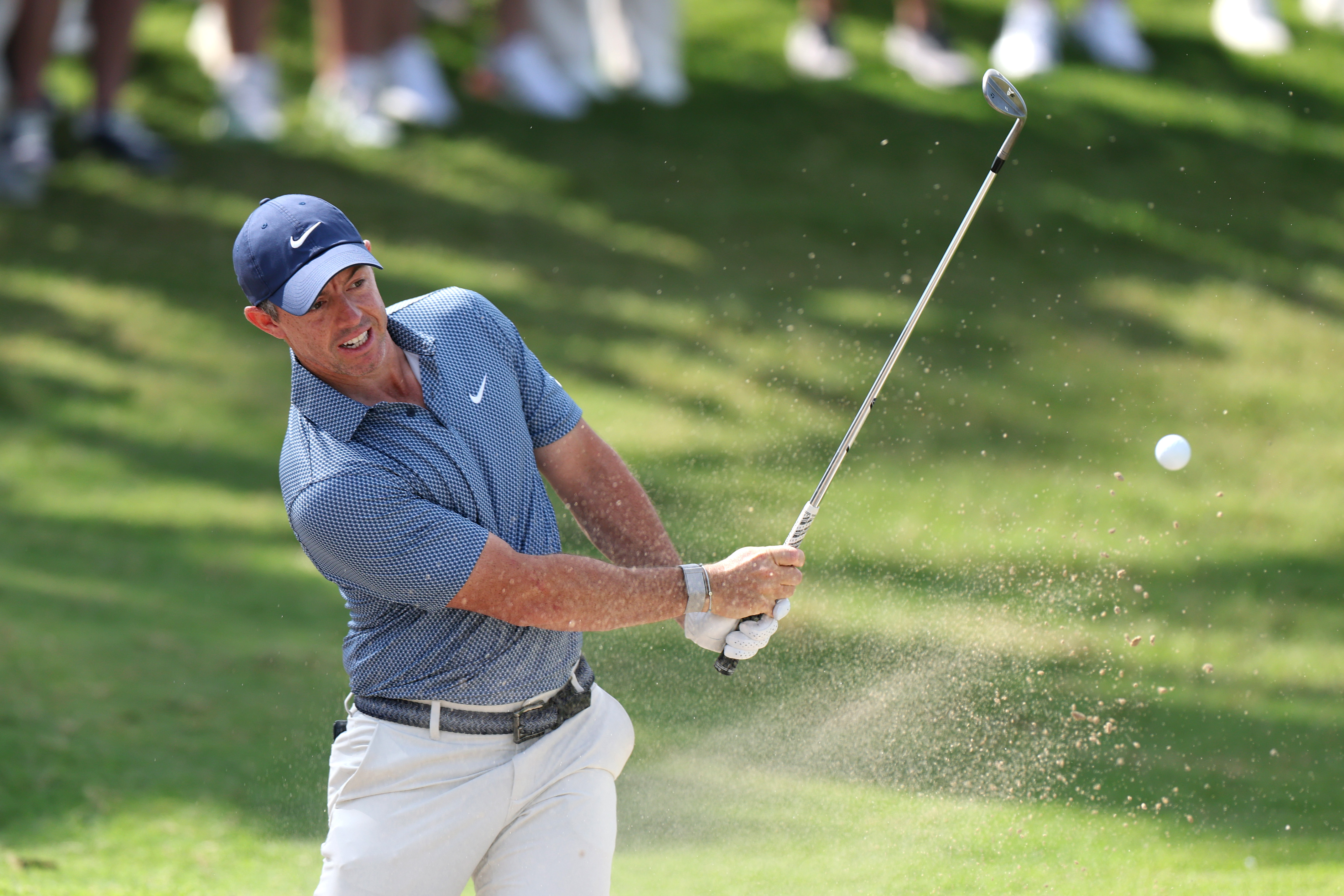 Rory McIlroy hitting a golf ball out of a sand bunker.