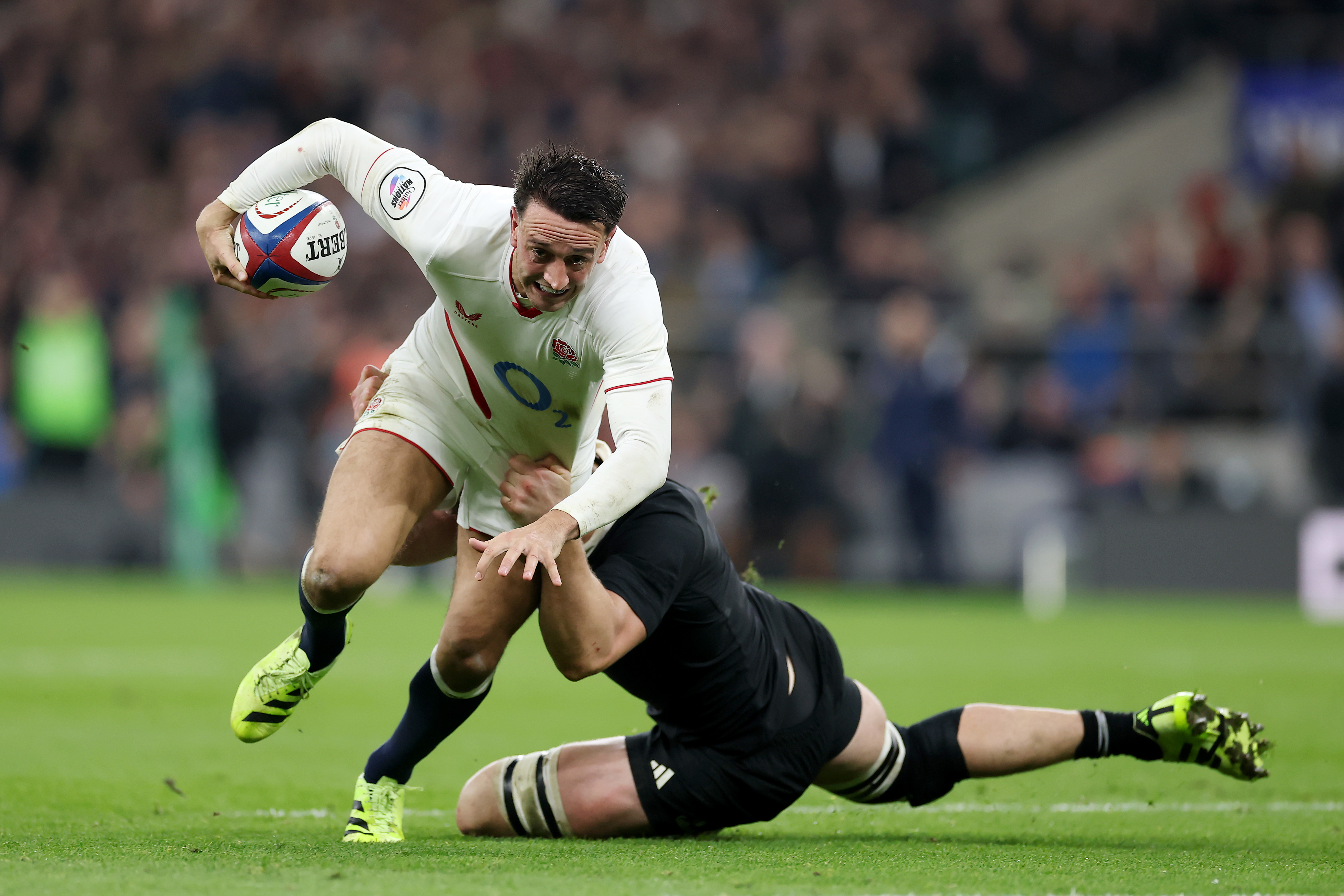 Alex Mitchell of England is tackled by Scott Barrett of New Zealand during a rugby match.