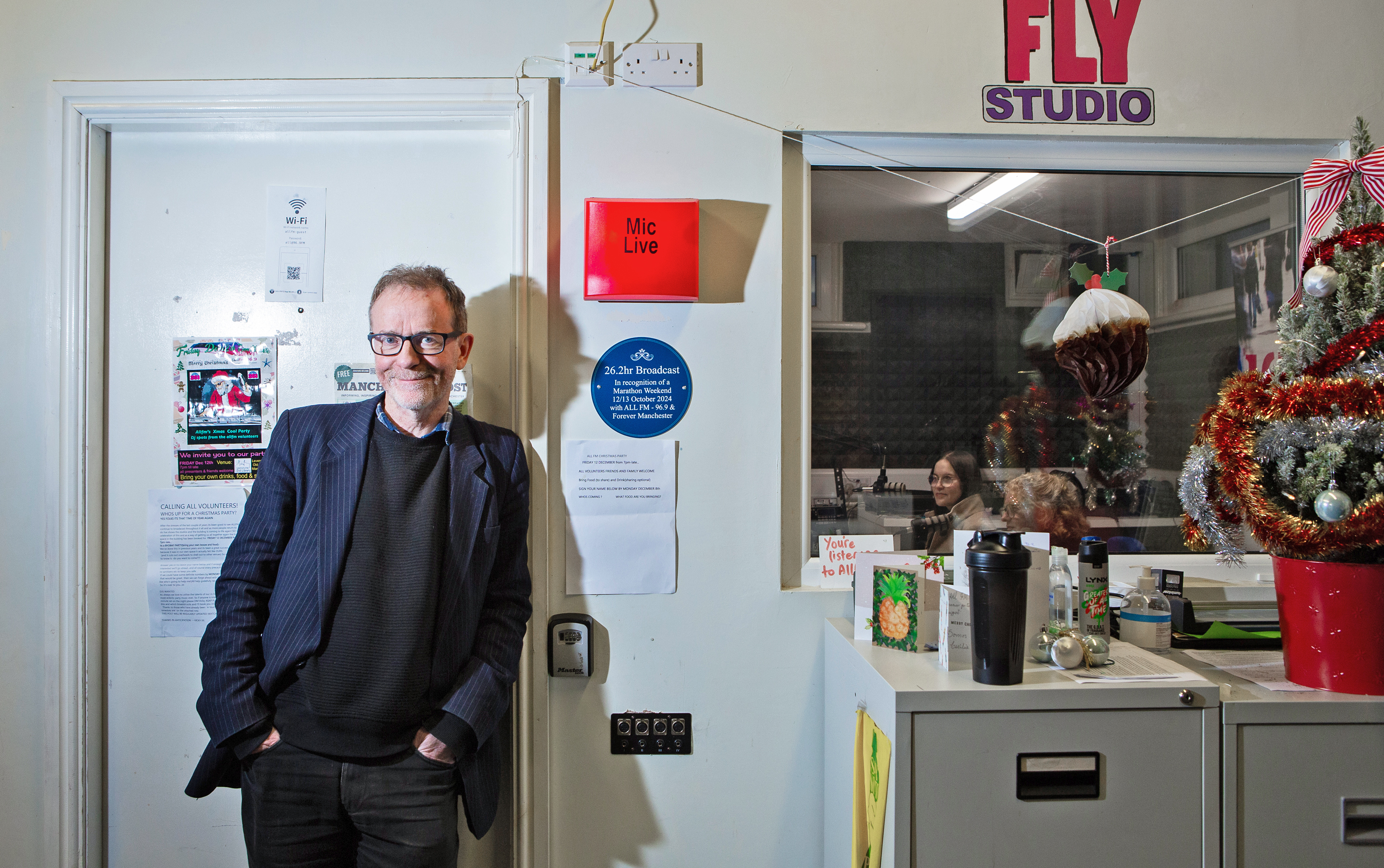 Director Ed Connole posing in front of Christmas decorations and a radio studio at All FM.
