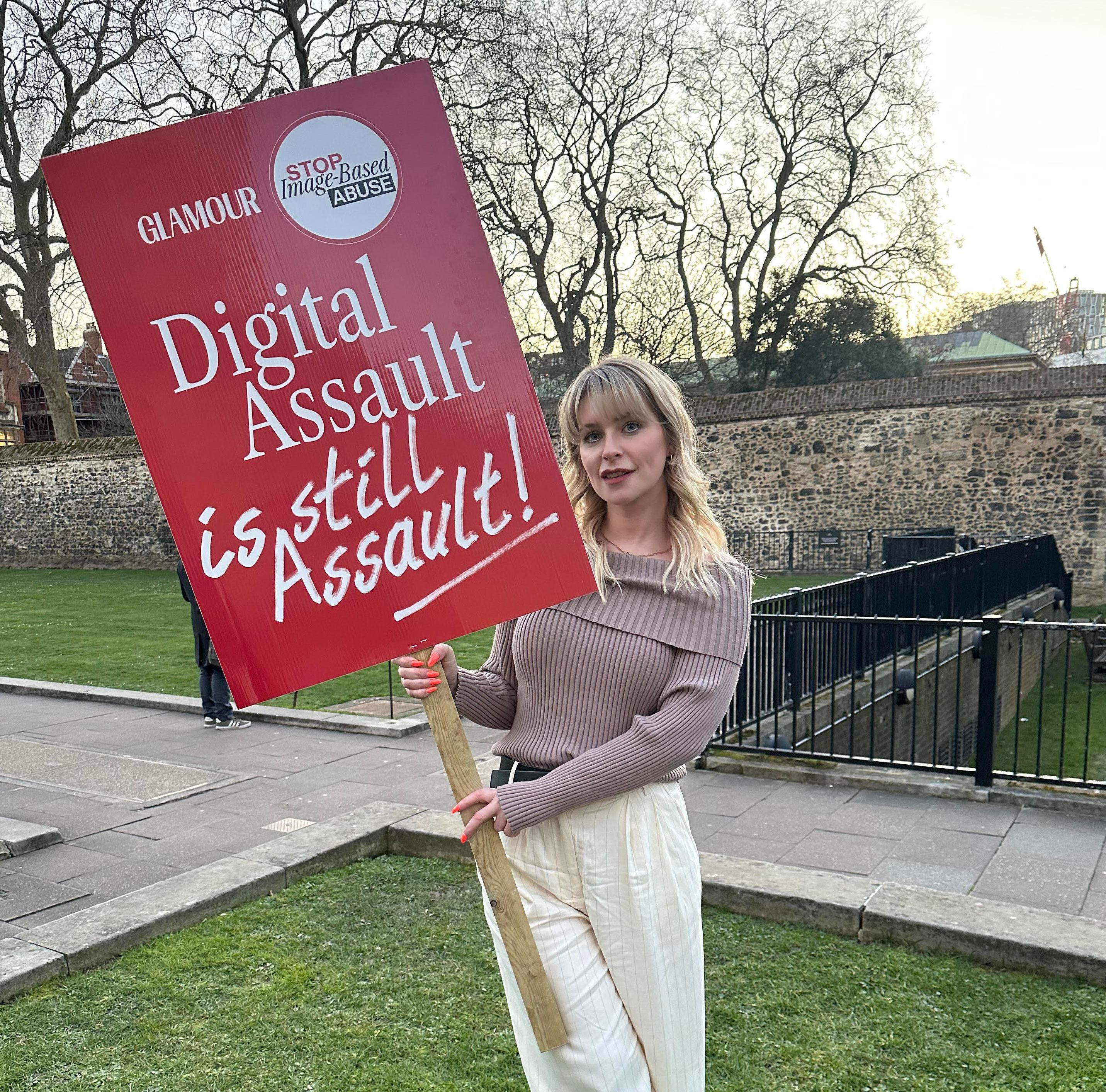 Jess Davies holding a red sign that says "Glamour Stop Image-Based Abuse Digital Assault is still Assault!"