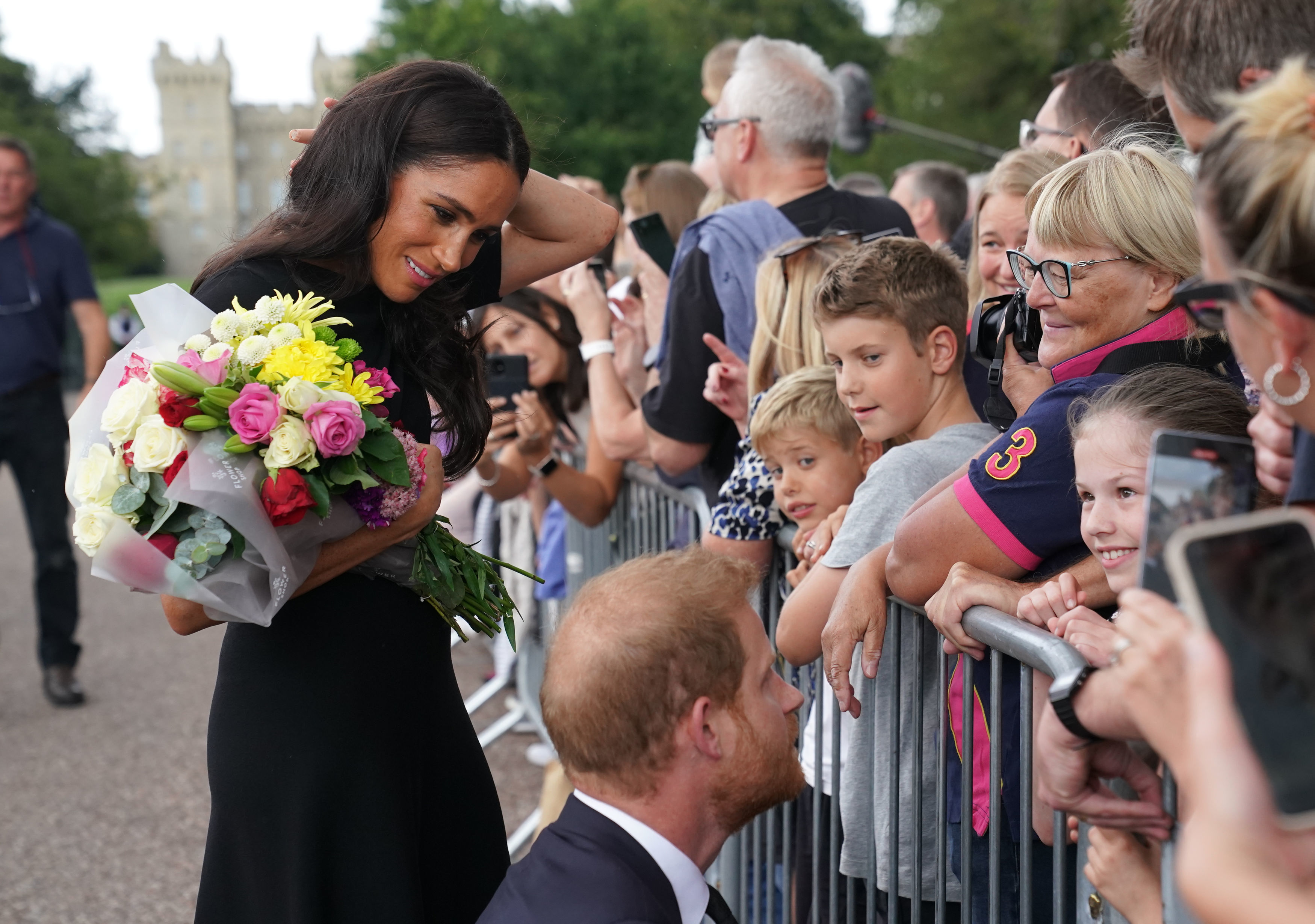 Meghan Markle holds a bouquet of flowers as she greets the public while Prince Harry speaks with children at Windsor Castle.