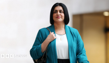 Home Secretary Shabana Mahmood arrives at the BBC in London. She is wearing a turquoise blazer and has a black handbag wrapped over her right shoulder