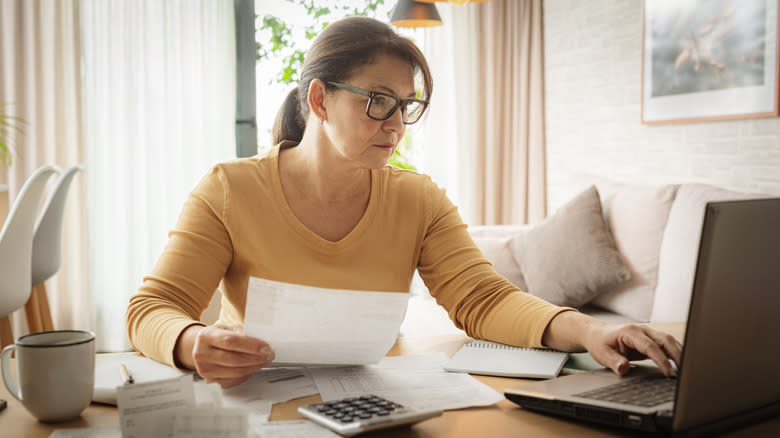 Woman working at a desk with a laptop computer, a calculator, and papers in her hand