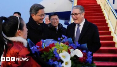Keir Starmer reacts with delight as he receives a bouquet of flowers at an airport in Beijing from a woman in a red costume with a white fur collar. Chinese Finance Minister Lan Foan reacts with a smile