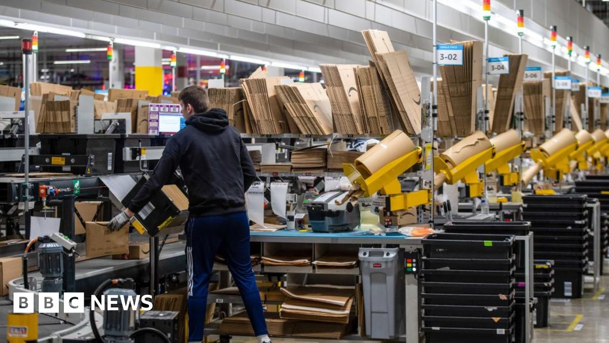 A worker at a warehouse packages items as they pass him on a conveyor belt.