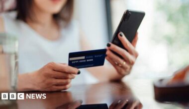 A woman is holding a credit card or debit card and doing online shopping on a smartphone.