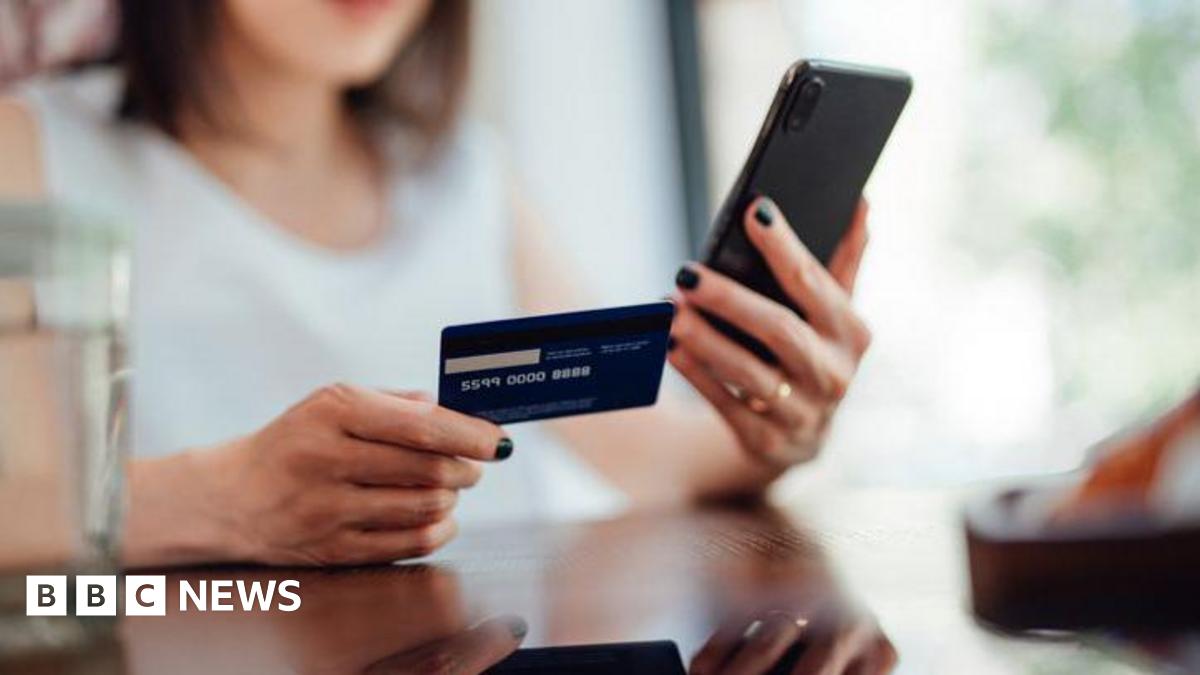 A woman is holding a credit card or debit card and doing online shopping on a smartphone.