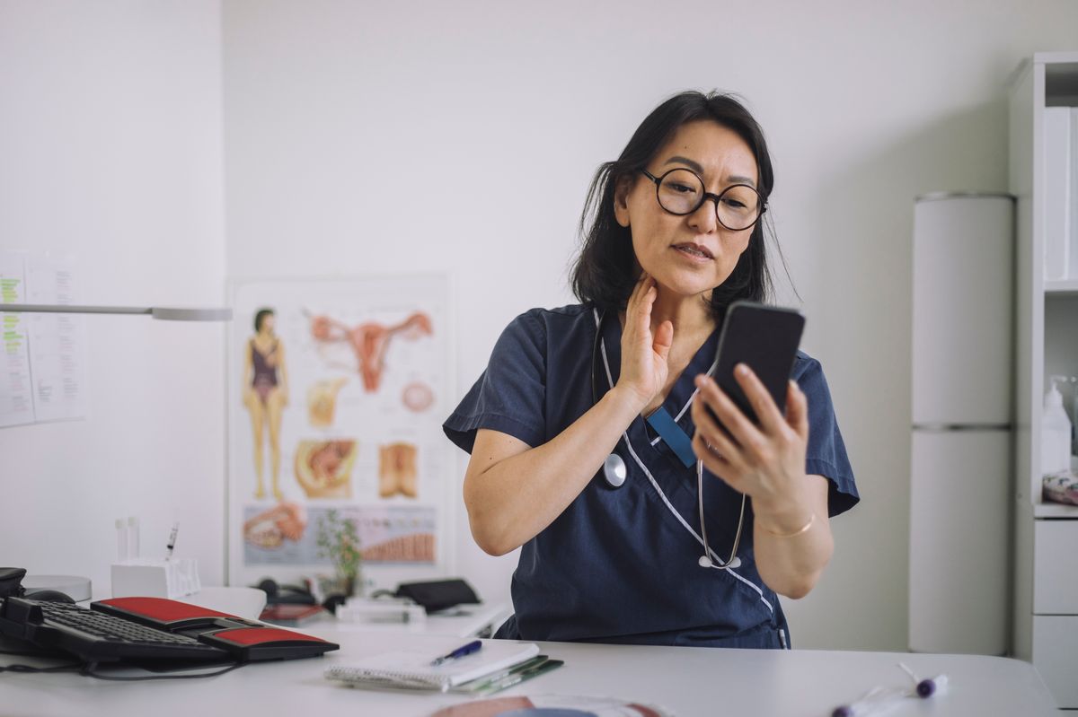 Female otolaryngologist doing online consultation through mobile phone while sitting at desk in medical clinic - stock photo