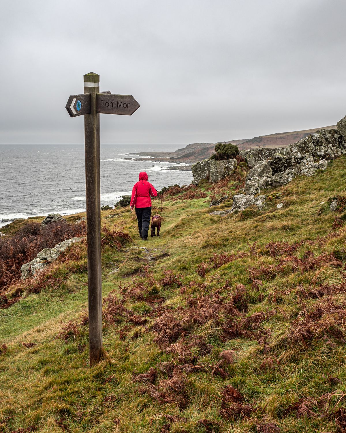 A lady in red walking her dog on Blane Way in Bute Scotland on a wet day