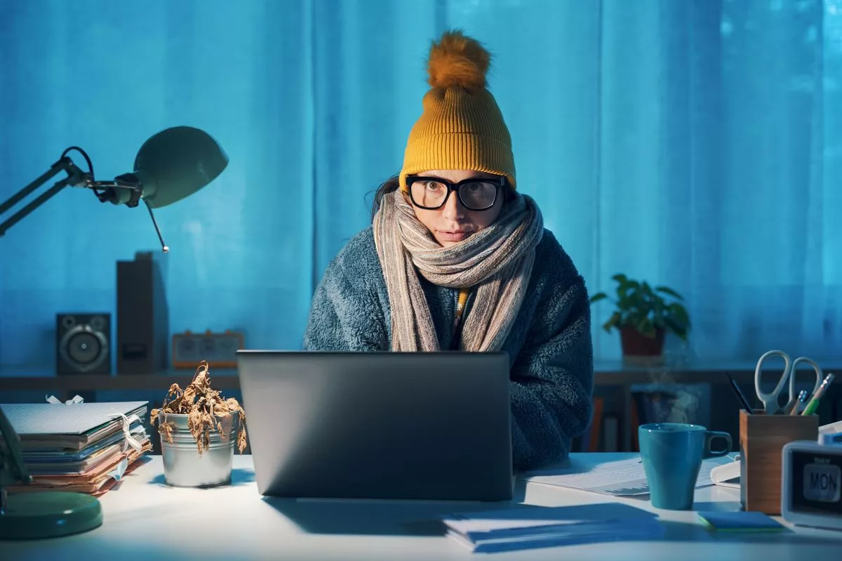 Woman sitting at desk and feeling cold, she is wearing warm clothes and saving money on her utility bills