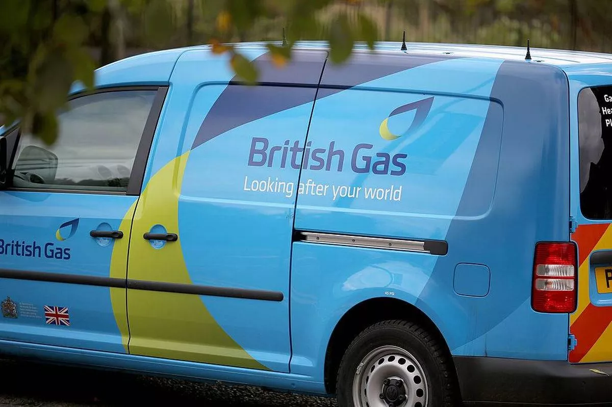 A blue utility van with the words "British Gas" prominently displayed on the side is parked on a road with greenery in the background. The vehicle features a distinctive yellow and blue design on its side panel.