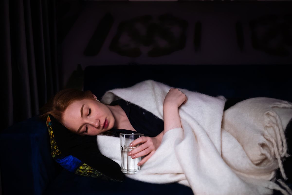 A woman rests on a sofa with a blanket, conveying a sense of peaceful tiredness. Her relaxed posture and calm expression, paired with soft lighting, capture a moment of serenity and quietude.