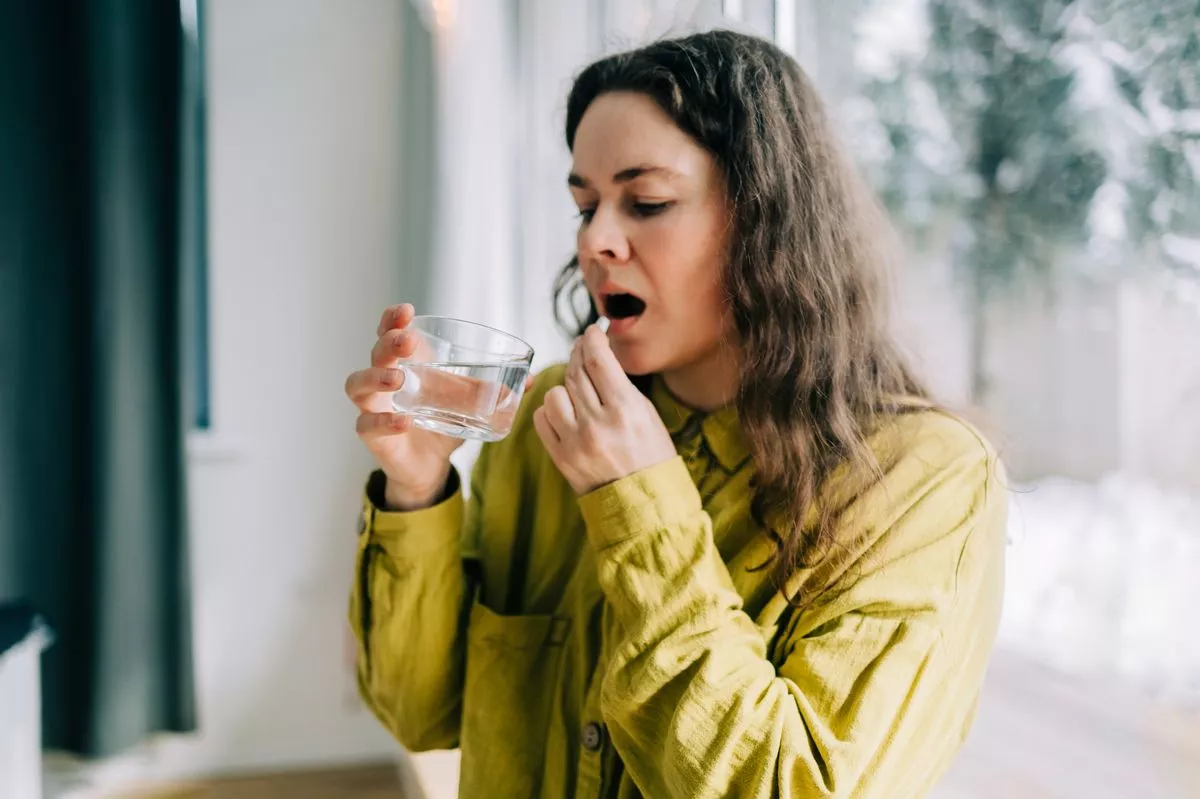 Mid woman taking medicine with glass of water at home