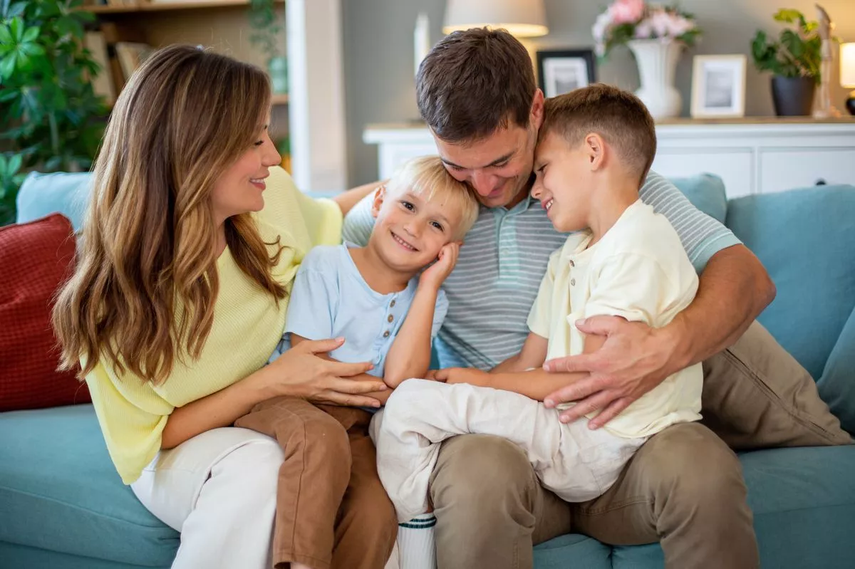 Parents and two happy sons hugging and smiling on a sofa at home, enjoying family time