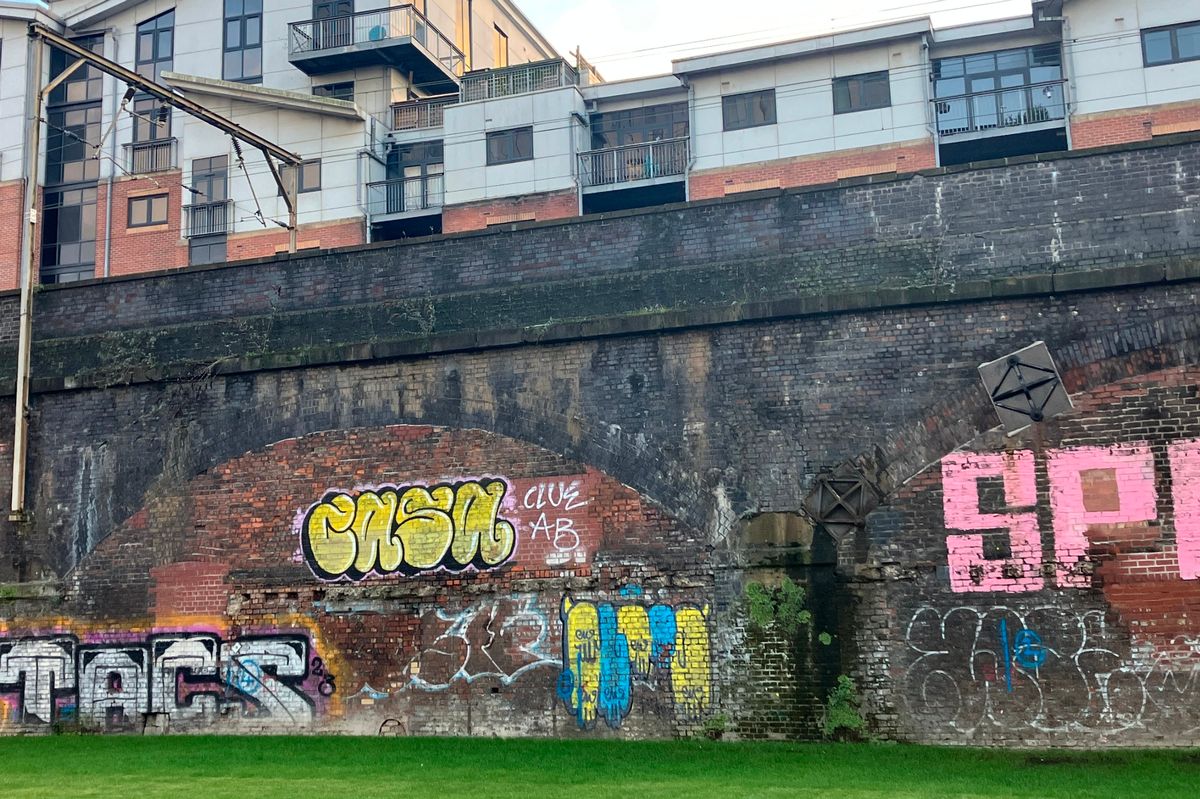 Graffiti on a wall beside a path of inaccessible grass, Whitworth Street West