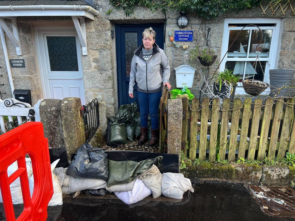 Anne Oliver outside her sandbagged home in Foundry, Stithians, and a stream of raw sewage, faeces, sanitary products, toilet paper and even hypodermic needles has been flowing past and into her homes three times in two weeks