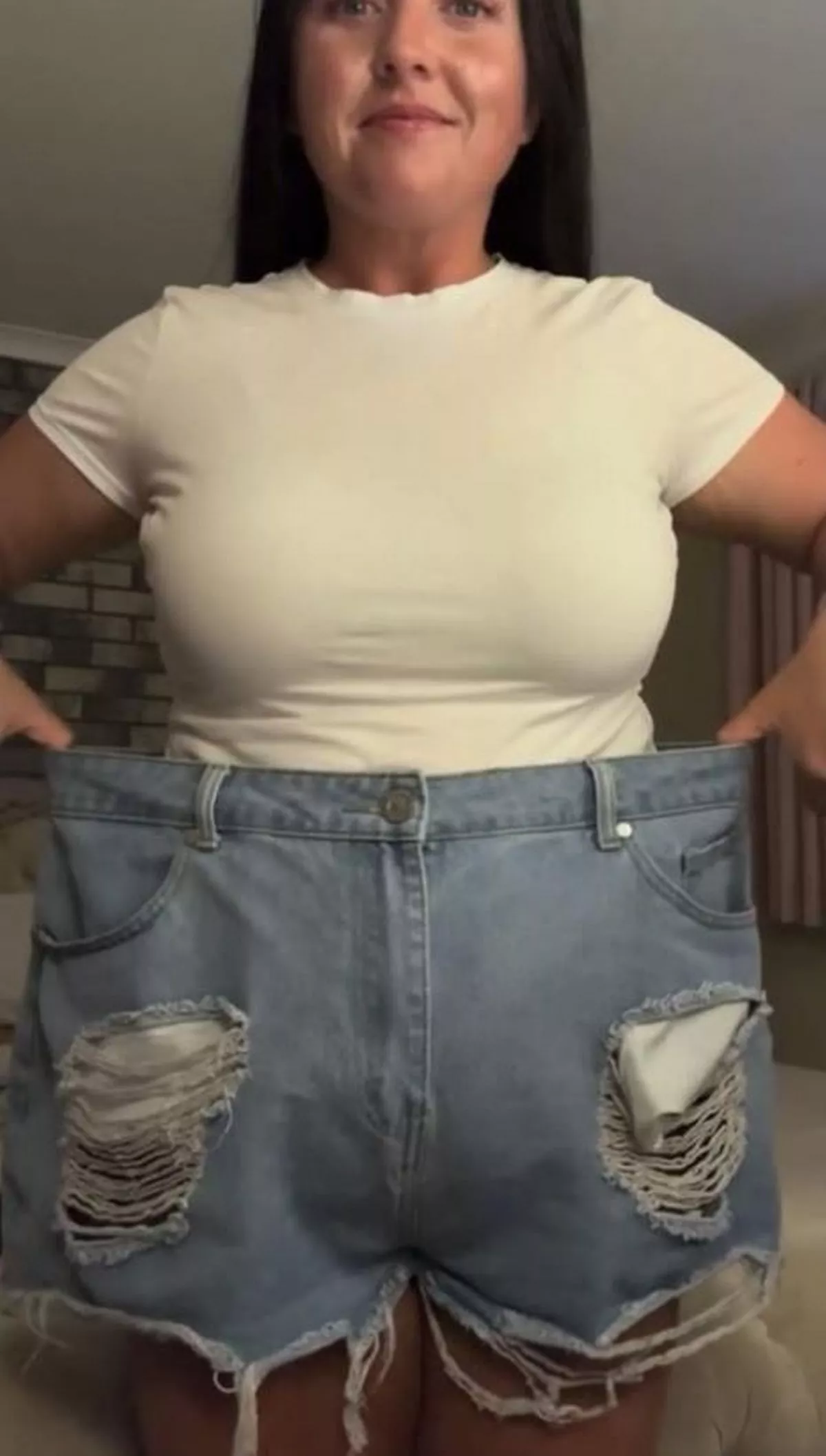 A dark-haired woman holding up oversized shorts to her waistline