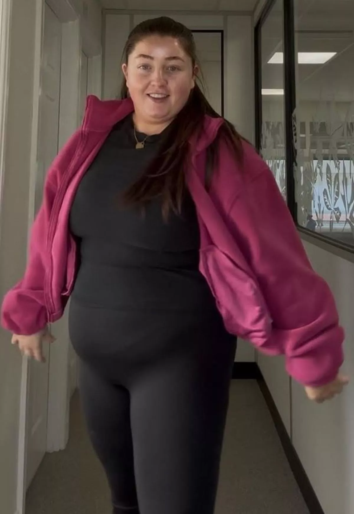 A brunette woman in black gym gear and a pink jacket