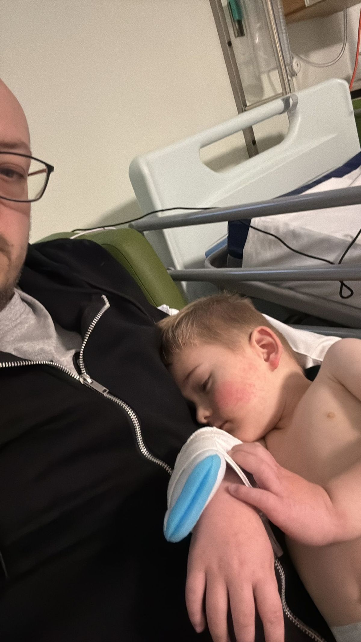 A man lying in a hospital bed, a little boy lying beside him sleeping