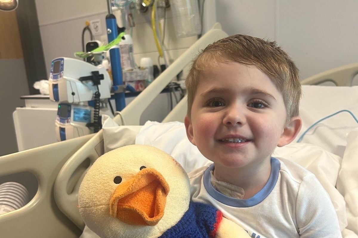 A young boy of three sitting up in a hospital bed smiling