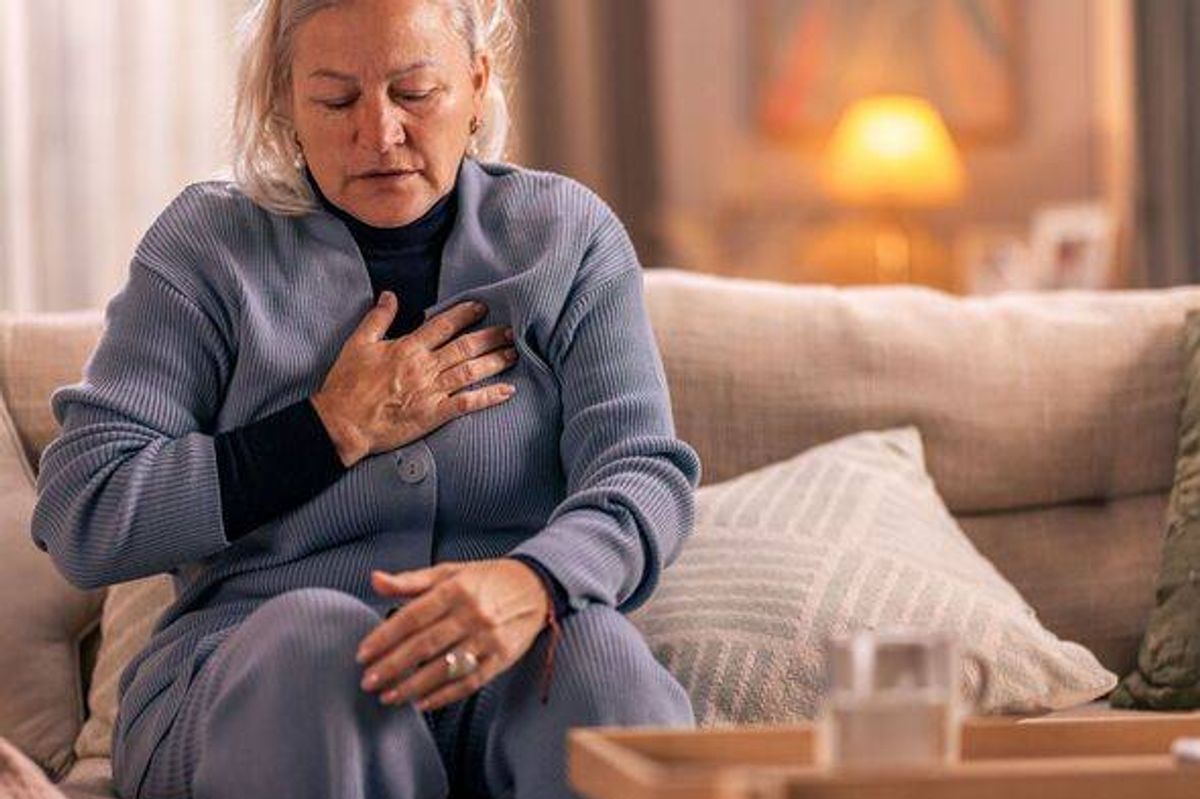Senior woman feeling chest pain while sitting on the couch at home