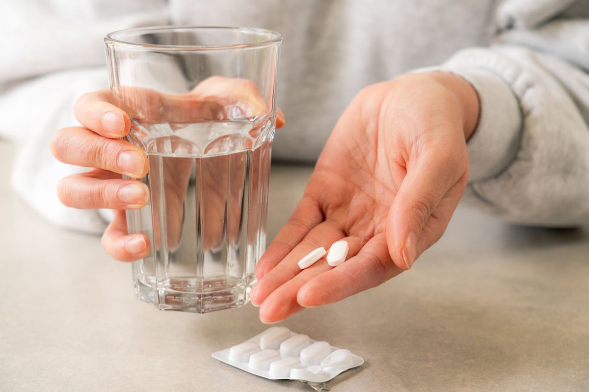 Woman holding pills in hand with glass of water