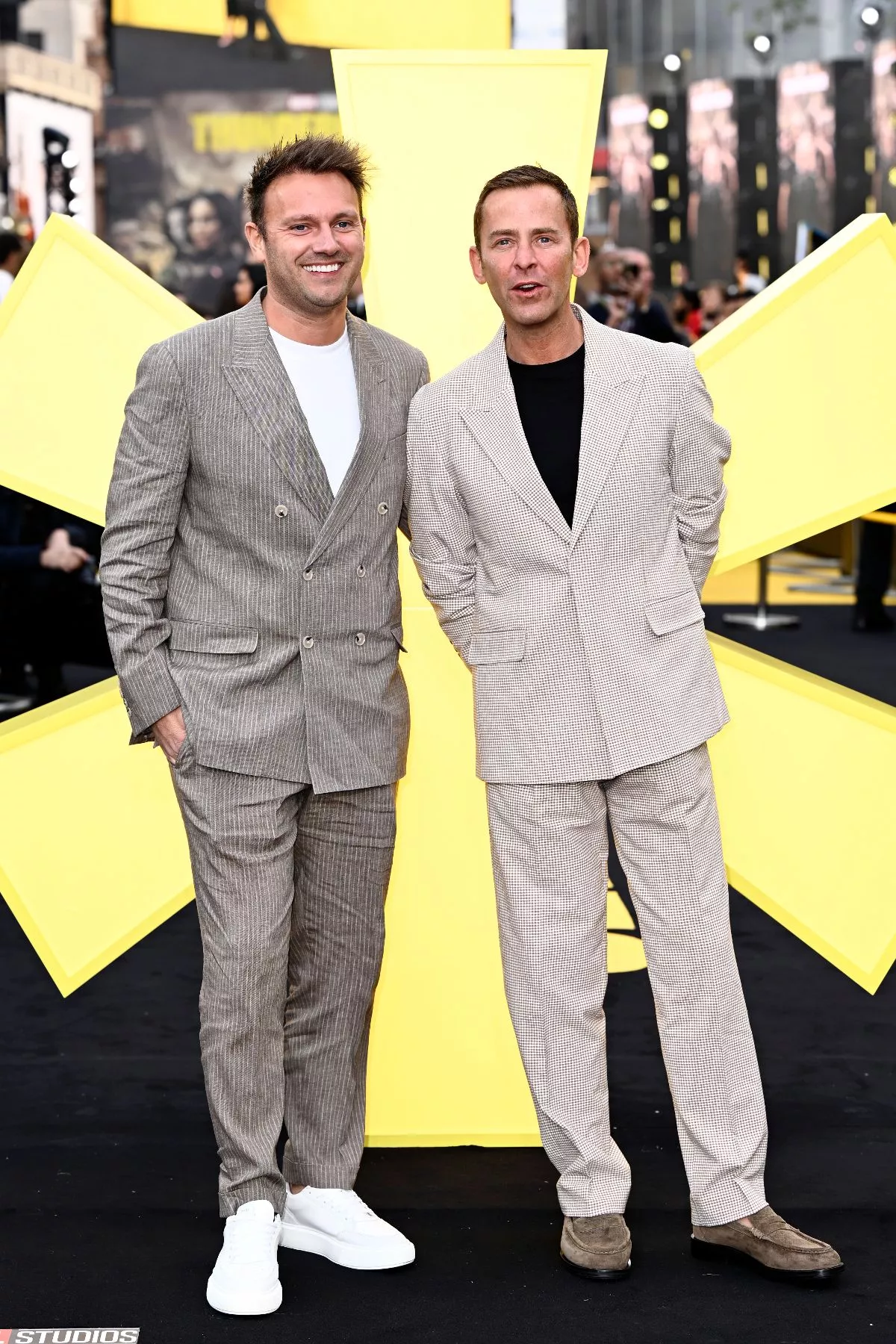 Two men on a black carpet even wearing cream suits