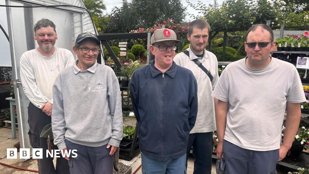 Five men, varying in age, standing in a row in front of stand of plants
