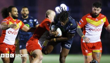 Wigan Warriors forward Junior Nsemba (centre) is tackled by a Sheffield Eagles player with two other Eagles players watching on from either side