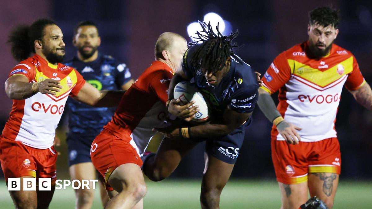 Wigan Warriors forward Junior Nsemba (centre) is tackled by a Sheffield Eagles player with two other Eagles players watching on from either side