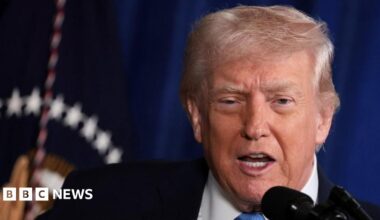 Venezuela's Vice-President Delcy Rodriguez presents the government's 2026 budget proposal to the National Assembly on 4 December 2025. She is wearing a salmon-coloured jacket and glasses. She is pointing with one hand and holding papers in the other.