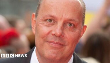 A close up of a man in a black suit and white shirt.