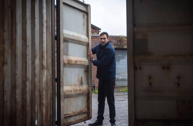Kit opening the door of a shipping container in Corrie