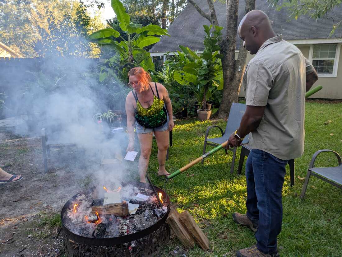 Dr. Elyse Stevens and a family member are standing near a backyard fire pit. She is putting prescription paper into the smoky fire.