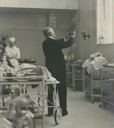 William Halsted in an operating room holding up an X-ray.