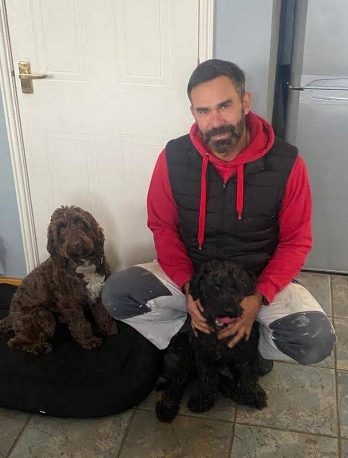 A man with dark hair kneeling down with two dogs