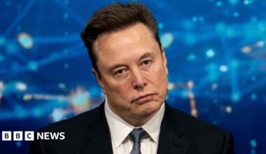 Elon Musk looking off camera in front of a blue background