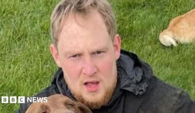 Police mugshot of Rhys Jamieson. He has a droopy left eye, scruffy hair and beard, grey t-shirt