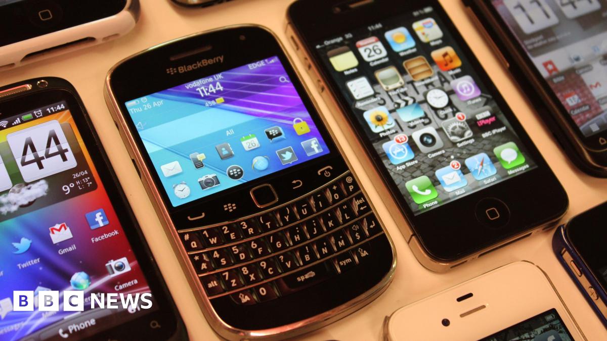 An Android smartphone, a Blackberry, and some iPhone, all unlocked with their screens on, spread out across a white table